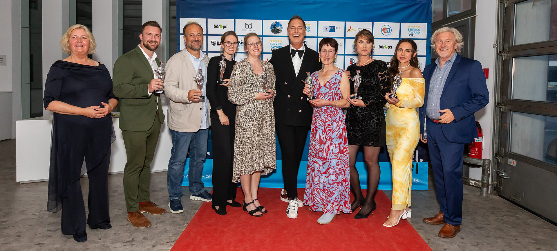 Gruppe von Gewinner*innen vor der Sponsorenwand beim Service Award Kiel 2024